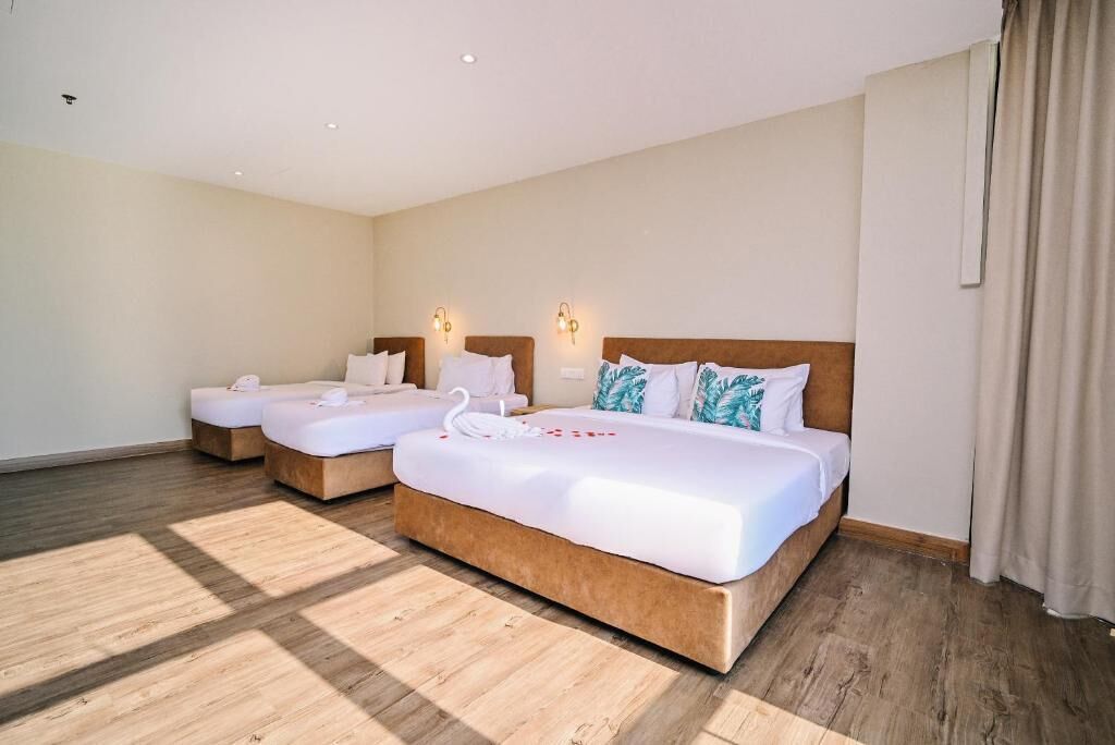 A hotel room with two beds, a wooden floor, and wall-mounted lights.