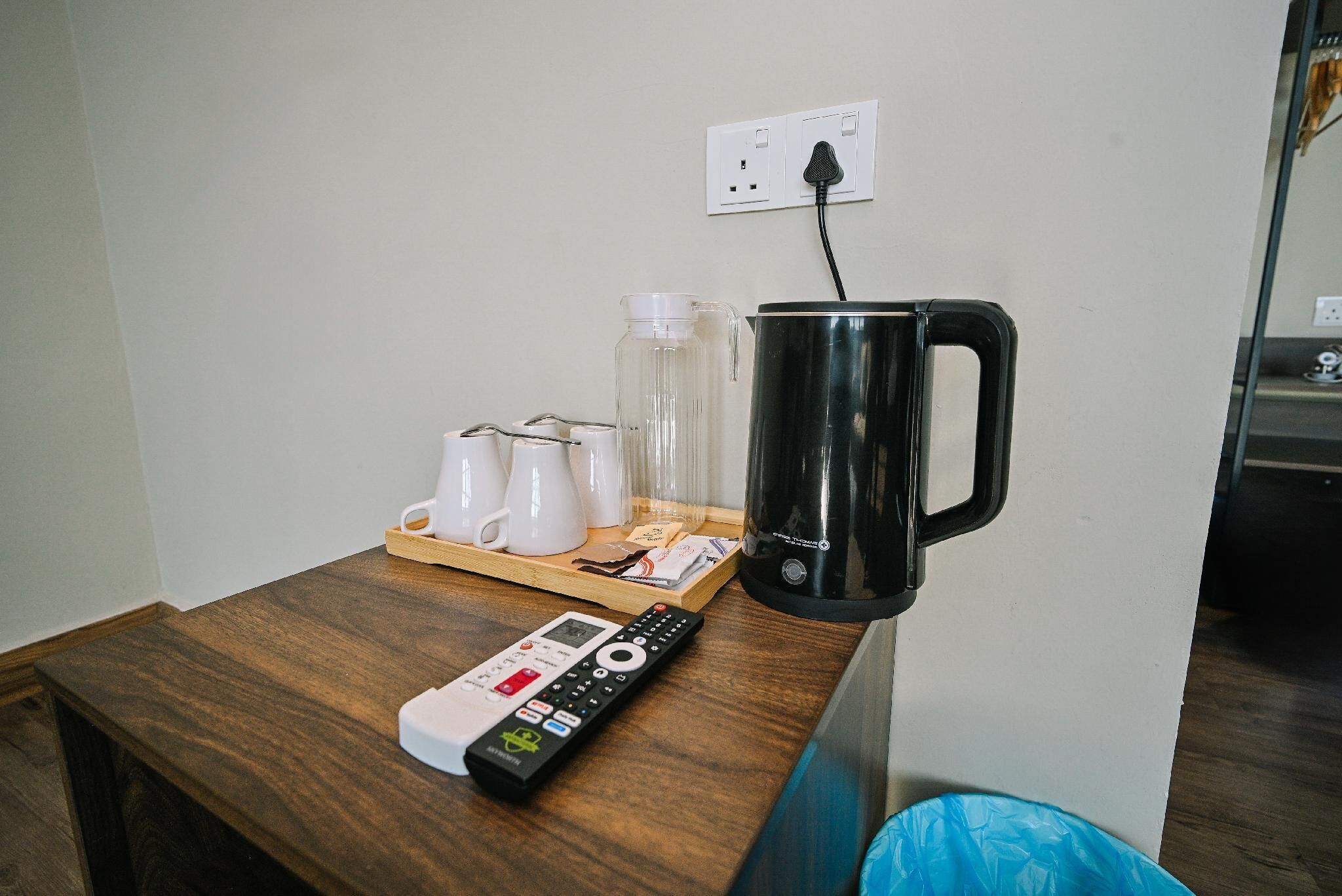 A wooden table with a coffee maker, a remote control, and a tray with cups and a glass.