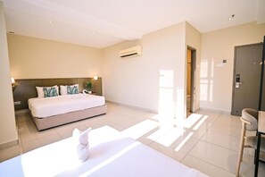 Quarto de hotel com cama, mesa de cabeceira e porta.