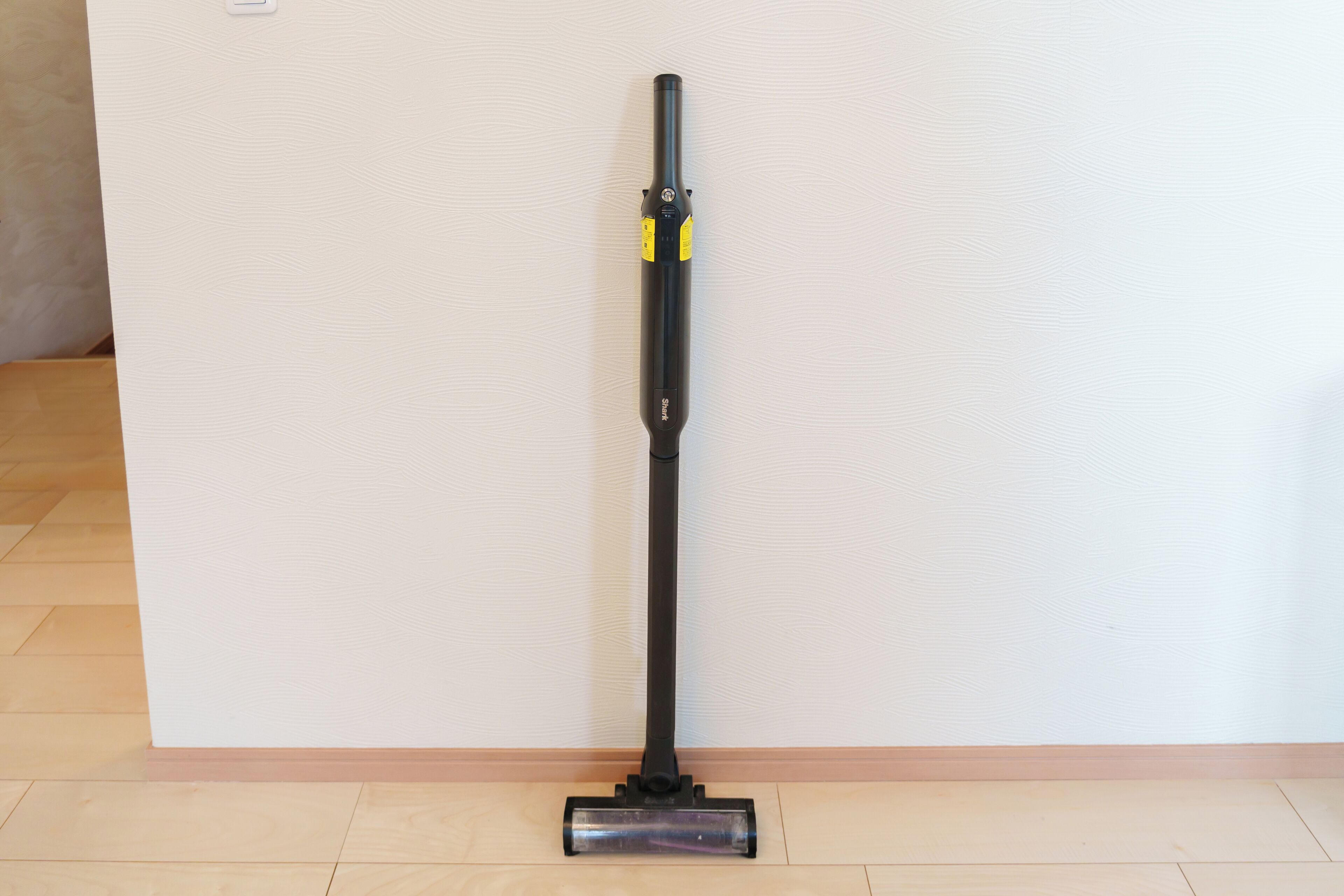 A vacuum cleaner standing upright against a wall with a wooden floor.