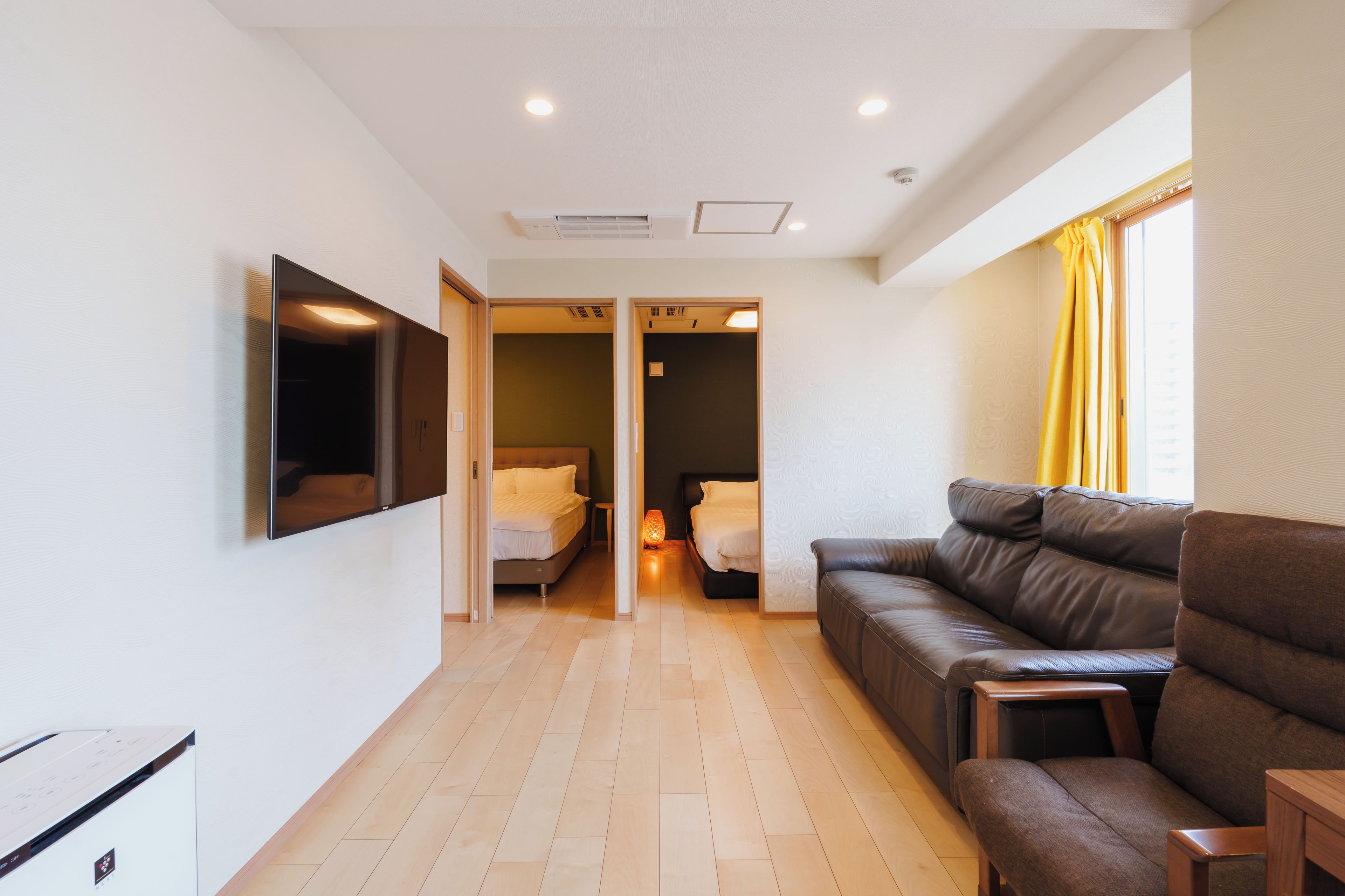 A modern hotel room with a sofa, a bed, and a TV mounted on the wall.