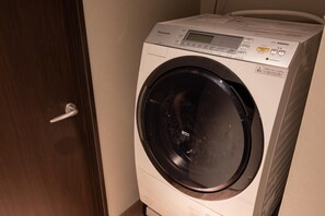 A front-loading washing machine with a digital control panel, a door handle, and a plastic bag on the right side. - Imakusa-so, Osaka, Dotonbori - Goyakuya - (大阪市中央区道頓堀１丁目東)