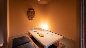 Una habitación con una mesa baja dispuesta para comer, un cojín y un jarrón decorativo en la pared.