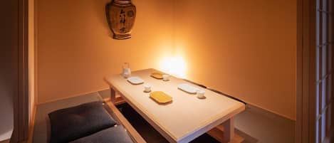 A room with a low table set for dining, a cushion, and a decorative vase on the wall.