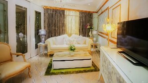 A living room with a sofa, a television, a chandelier, and a large window with curtains.