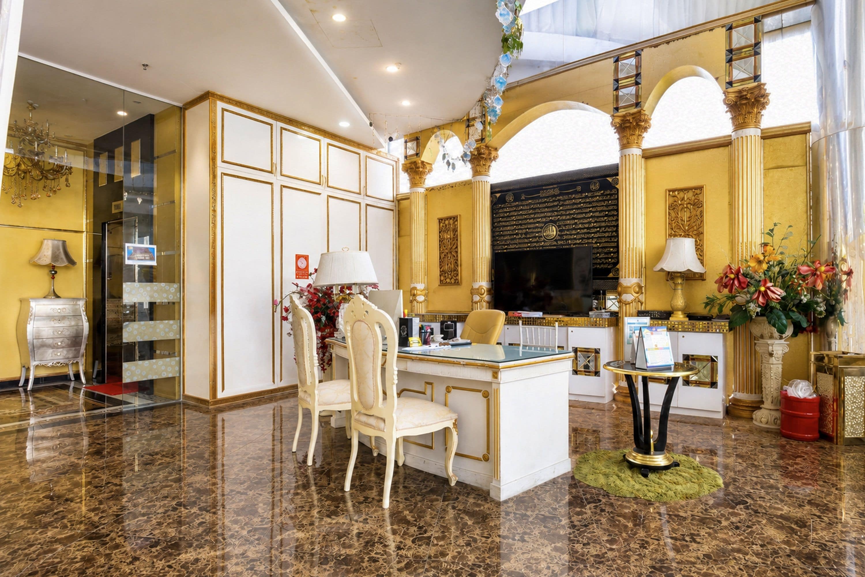 Un lobby de hotel lujoso con suelo de mármol, una recepción, una zona de estar con sillas y un espejo decorativo grande.
