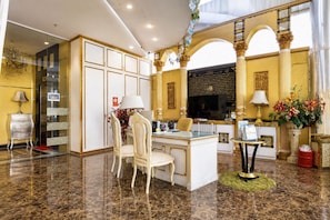 Una lussuosa hall d'albergo con pavimento in marmo, una reception, un'area relax con poltrone e un grande specchio decorativo.