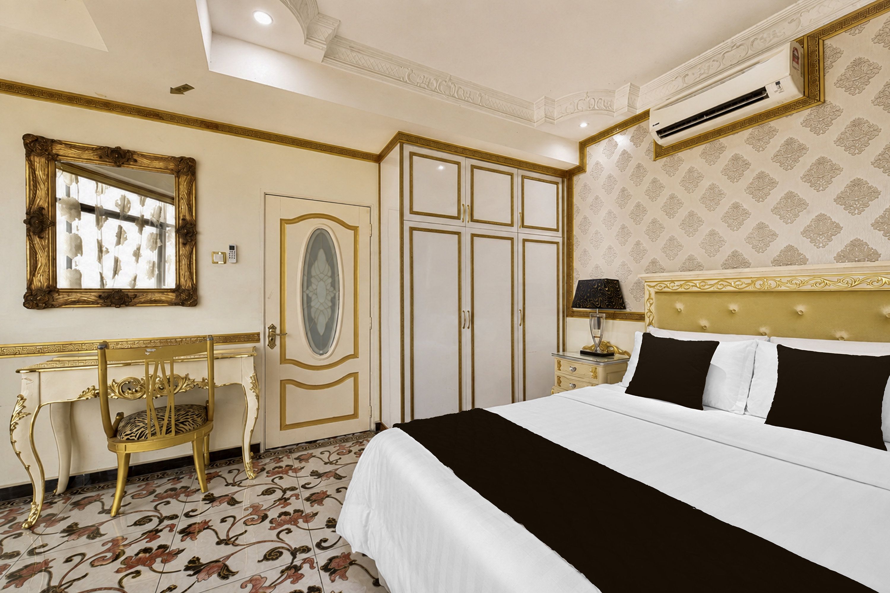 A hotel room with a bed, a vanity with a mirror, a chair, a wardrobe, and an air conditioning unit.