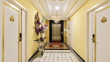 Corredor de hotel com lustre, tapete vermelho e elevador moderno.