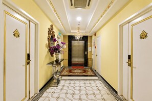 Corredor de hotel com lustre, tapete vermelho e elevador moderno.