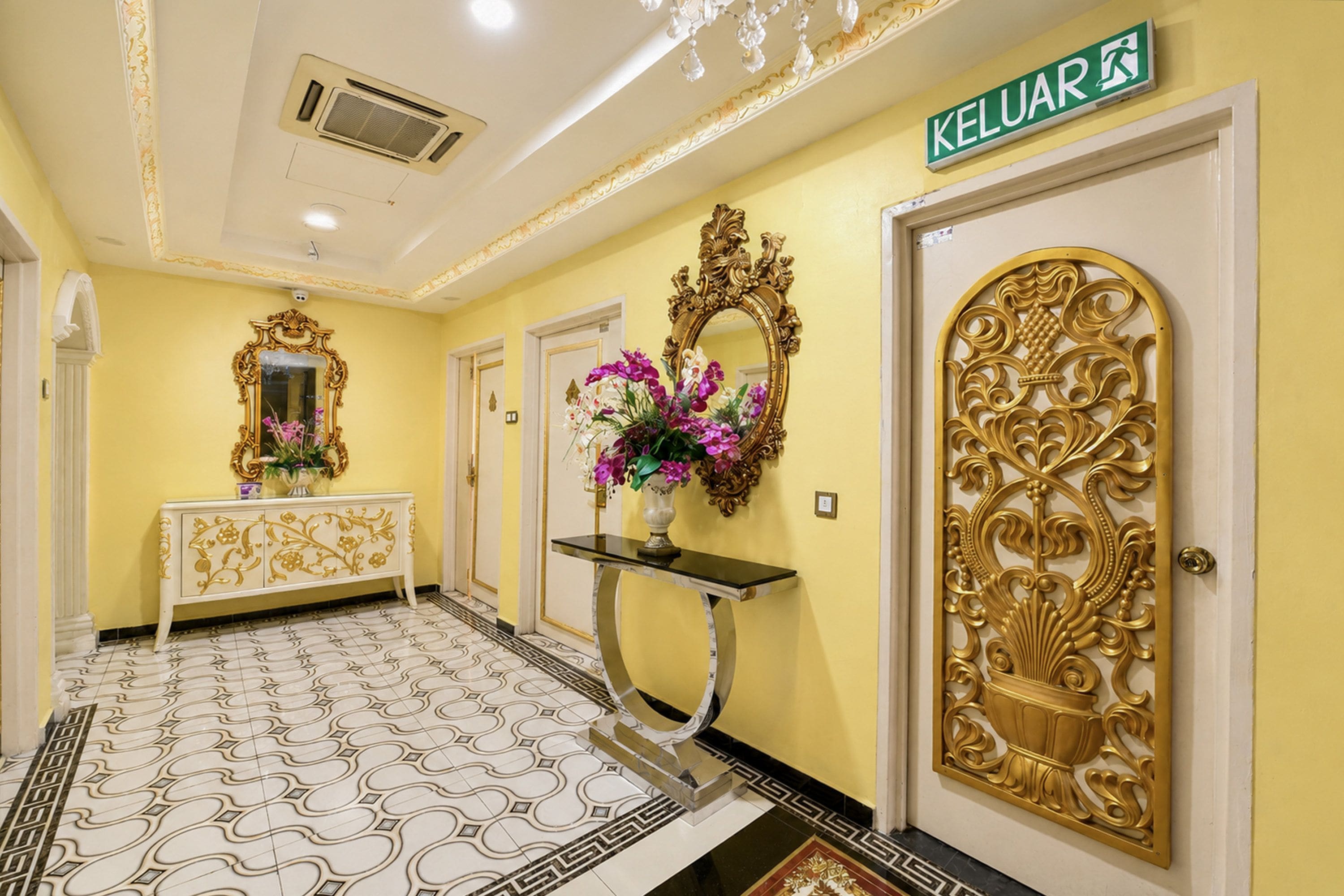 A hallway with a yellow wall, a white door with a gold design, and a sign reading 'KELUAR'.