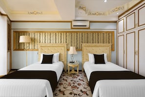 Camera d'albergo con due letti, un tavolino, una lampada e un pannello decorativo a parete.