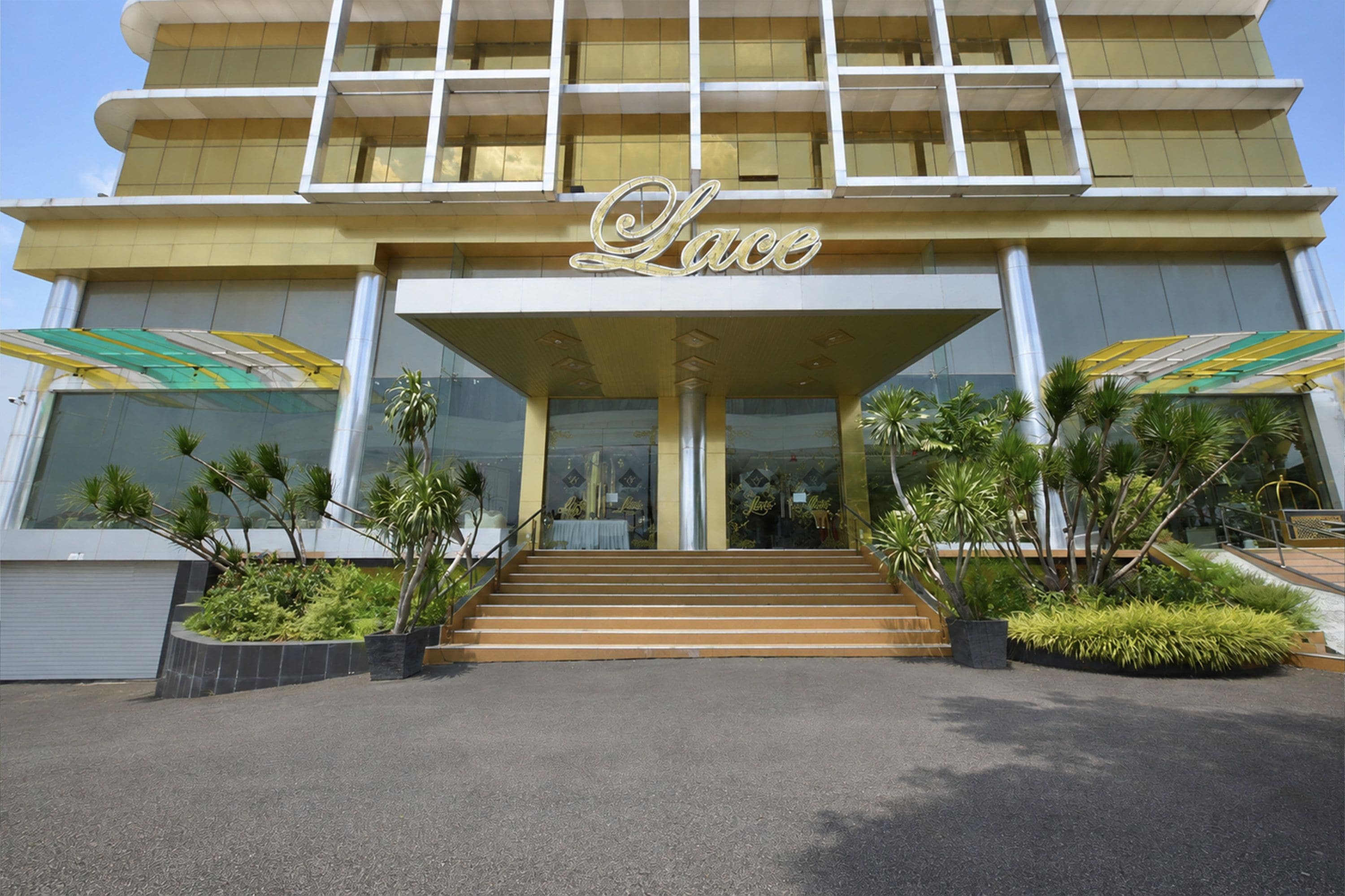 A hotel entrance with a sign reading 'Lace' above the doors, surrounded by greenery and a staircase leading up.