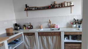 A kitchen with a wooden countertop, a built-in sink, and a backsplash with a unique pattern. There are shelves above the countertop holding various kitchen items.