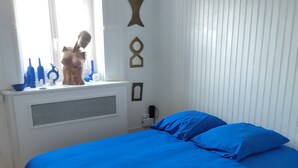 A bedroom with a large bed, a radiator, a window with decorative bottles, and wall-mounted artwork.