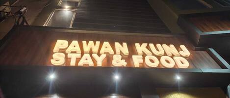 A hotel sign with 'PAWAN KUNJ STAY & FOOD' illuminated.