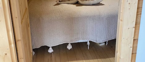 A wooden cabin room with a bed, pillows, and a hanging light fixture.