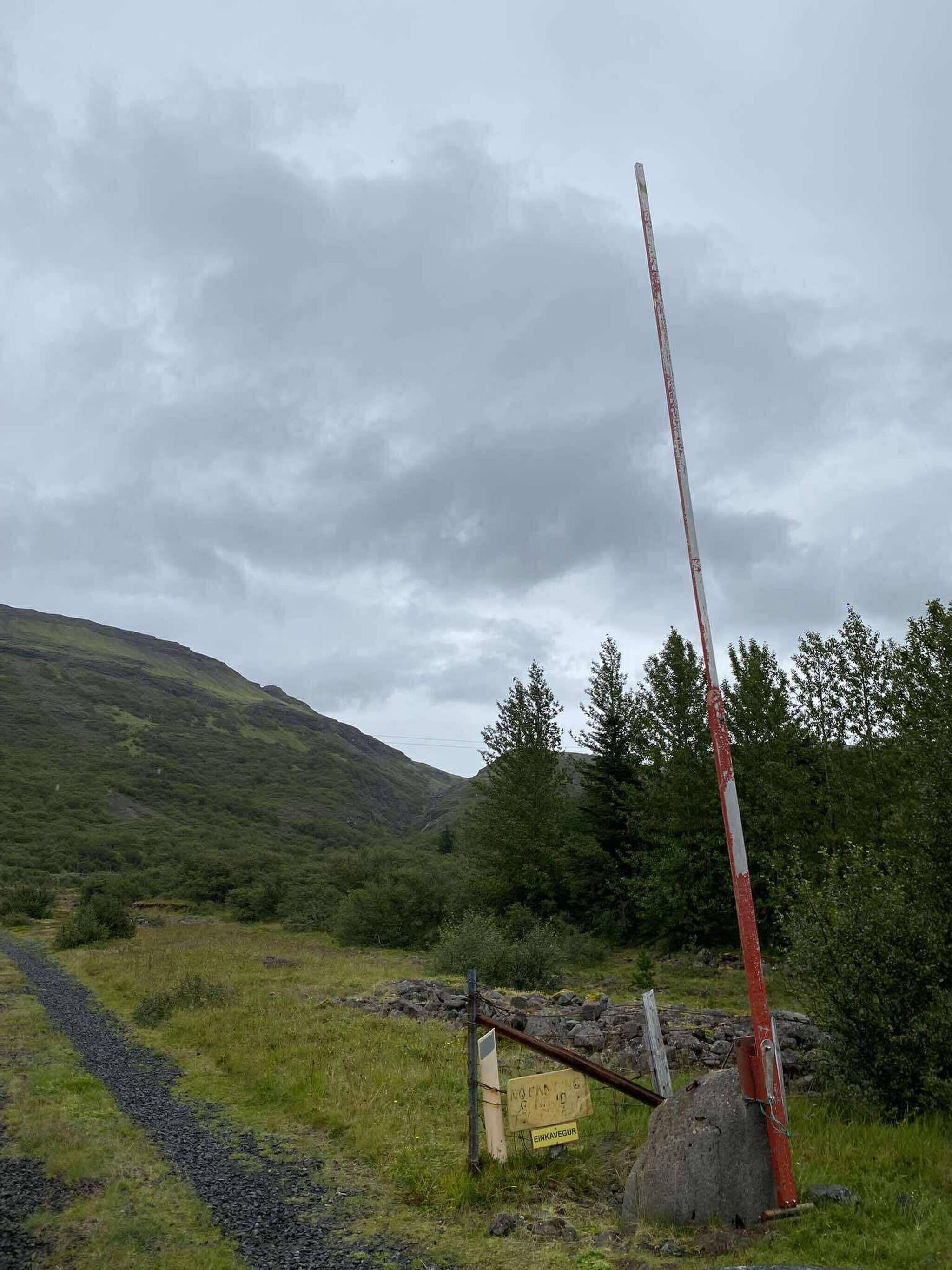 A rural landscape with a grassy path, a wooden structure, and a red and white pole.