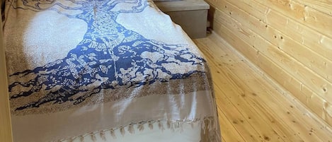 A wooden cabin room with a bed, a nightstand, and a hanging light fixture.