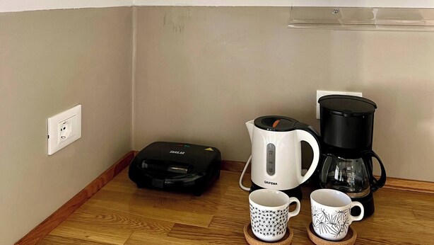 A kitchen with a coffee maker, a kettle, and a microwave on the counter. There are two mugs on coasters.