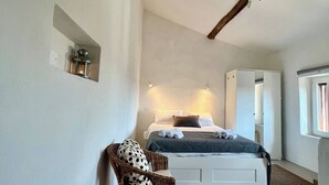 A bedroom with a bed, a chair, a bedside table, and a window.
