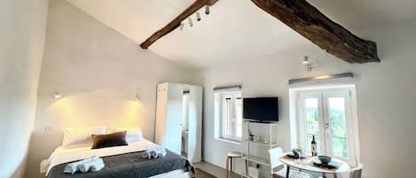 A bedroom with a bed, a desk, a chair, a television, and a window.