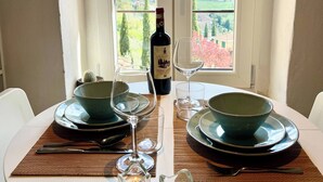 A dining table set with plates, glasses, and a bottle, with a view of a landscape through a window.