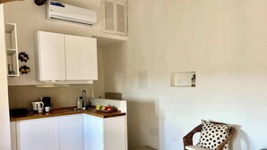 A compact kitchen with white cabinets, a wooden countertop, and a wicker chair with a polka dot cushion.