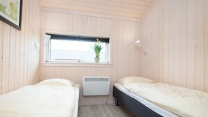 Pequeña habitación con dos camas, una ventana con una planta, un radiador y un aplique de pared.
