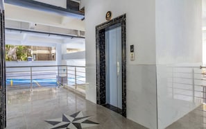 Un hall d’entrée propre et moderne, avec un sol en marbre, un motif décoratif en forme d’étoile, un ascenseur en verre et une rambarde en métal.