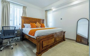 A bedroom with a wooden bed, a desk with a chair, a large mirror, and a window with curtains. - Cozy Nest 1BR Kilimani (Nairobi)