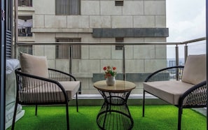 Un balcon avec deux chaises, une petite table et un vase de fleurs.