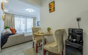 A modern living room with a sofa, two armchairs, a coffee machine, and a dining table set for two. - Cozy Nest 1BR Kilimani (Nairobi)