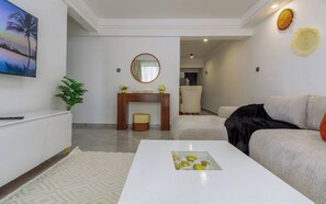 Un salon moderne doté d’un téléviseur à écran plat, d’une table basse agrémentée d’objets décoratifs, d’un canapé, d’une cheminée et d’un coin repas.