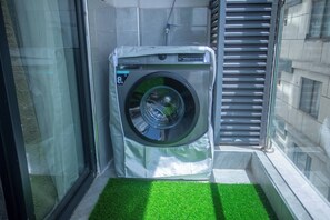 A compact, modern laundry room with a built-in washer and dryer, a small green artificial turf area, and a window with blinds. - Cozy Nest 1BR Kilimani (Nairobi)