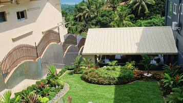 A residential property with a well-maintained lawn, a covered patio area, and a view of a lush green landscape with palm trees.