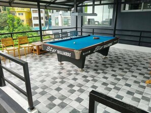 Una mesa de billar con la marca 'Star Billiards', rodeada de piso a cuadros, y una vista a un balcón con sillas y una mesa.