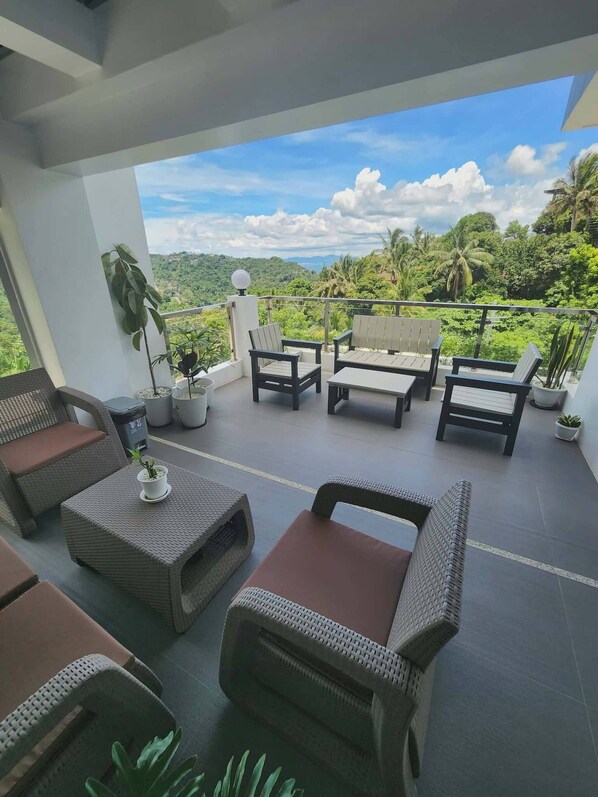 A balcony with wicker furniture, potted plants, and a view of a lush landscape.