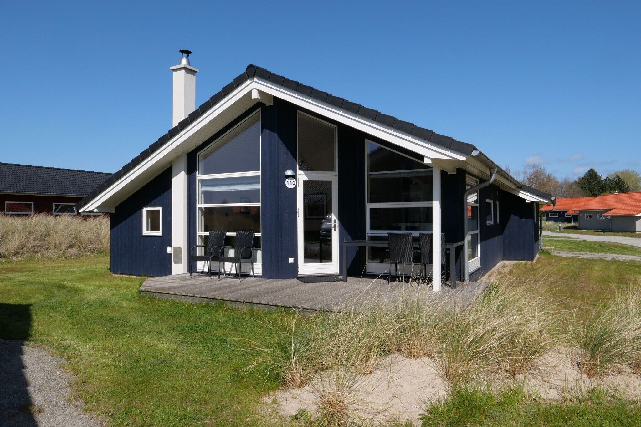 A modern house with a large open porch, a chimney, and a number 116 sign.