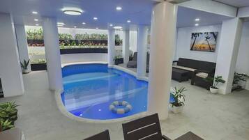 An indoor swimming pool with a curved design, surrounded by seating areas and potted plants.