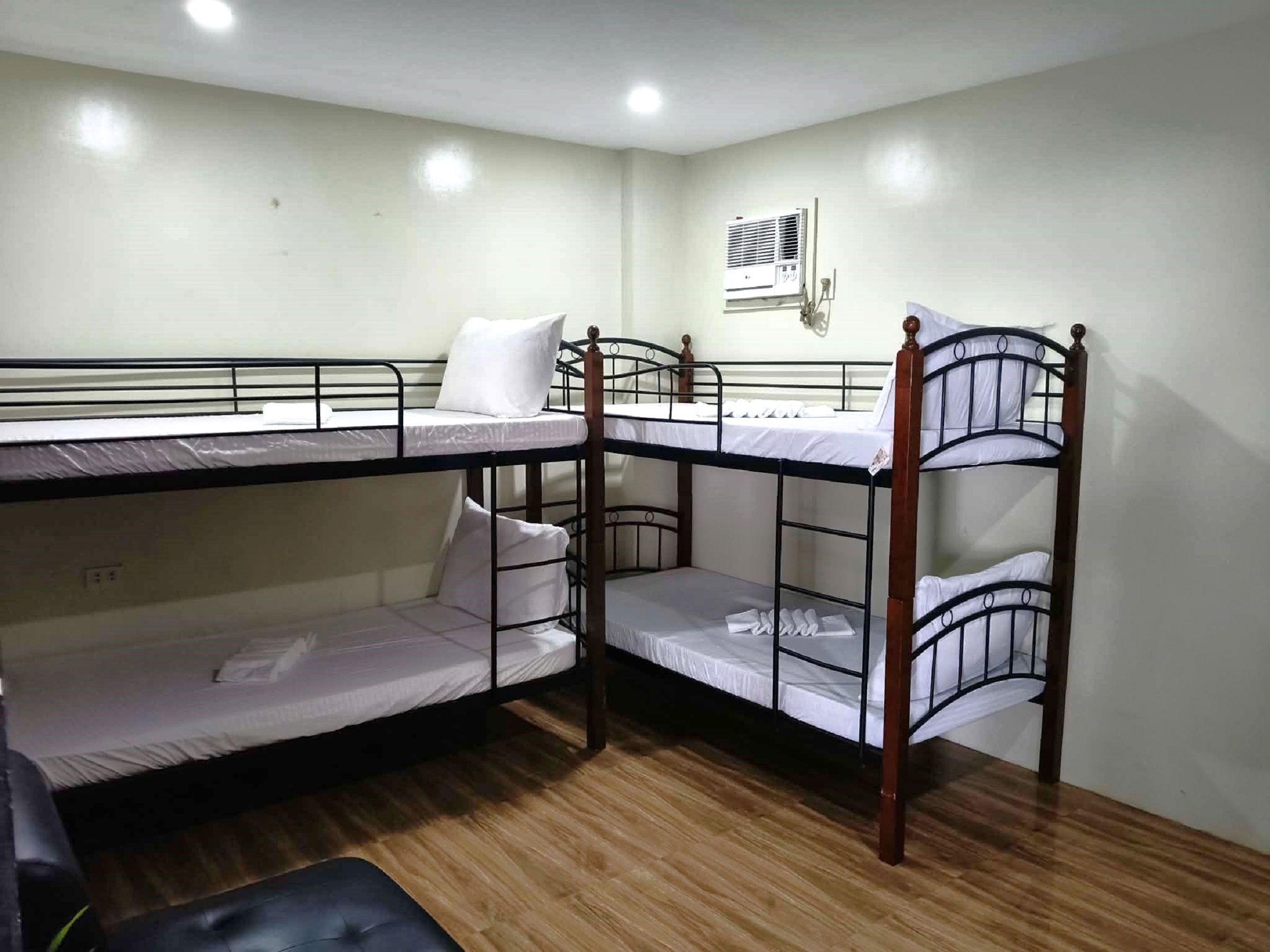 A bunk bed room with a wooden floor, a wall-mounted air conditioner, and a single bed with a pillow.