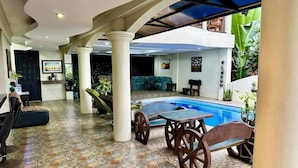 A pool area with a tiled floor, a table with chairs, and a sofa.