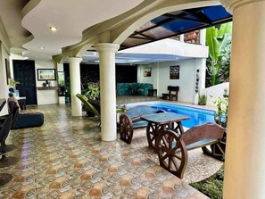 A pool area with a tiled floor, a table with chairs, and a sofa.