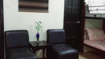 A room with a sofa, two chairs, a small table with a plant, a window with blinds, and a door.