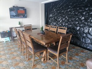 Un coin repas avec une table et des chaises en bois, un téléviseur fixé au mur et un mur noir à texture.