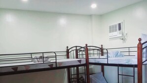 A bunk bed room with a wooden floor, a small seating area, and a wall-mounted air conditioning unit.