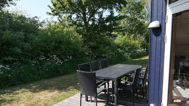 An outdoor patio with a table and chairs, surrounded by greenery. - Grobenbrode Beach Ferienhaus für 8 Personen (Großenbrode)