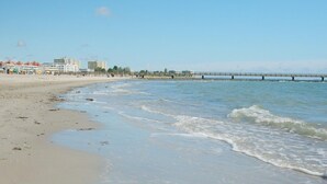 A beach with a pier extending into the water, buildings in the background, and a clear sky. - Grobenbrode Beach Ferienhaus für 8 Personen (Großenbrode)