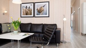 A modern living room with a black leather sofa, a white coffee table, a potted plant, and two framed pictures on the wall. - Grobenbrode Beach Ferienhaus für 8 Personen (Großenbrode)