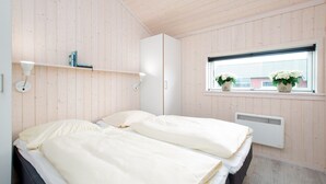 A bedroom with two beds, a window with potted plants, a radiator, and a shelf with books. - Grobenbrode Beach Ferienhaus für 8 Personen (Großenbrode)